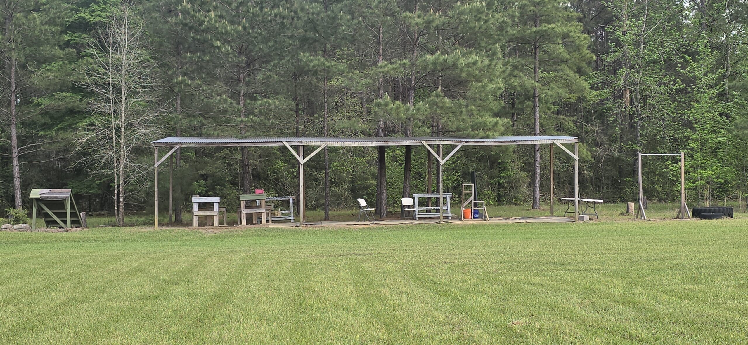 A covered outdoor structure in a clearing, backed by dense forest.