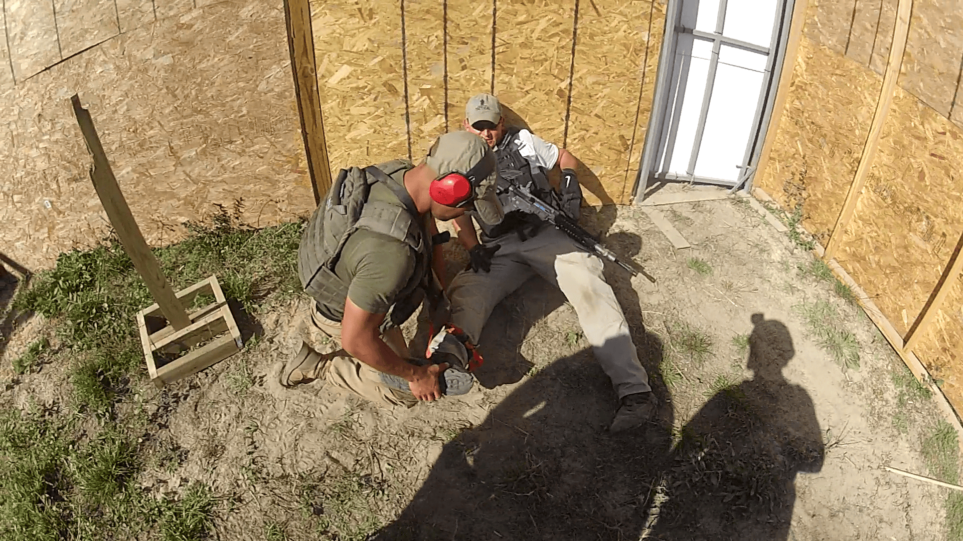 Two men are in a simulated tactical training scenario inside a plywood structure.